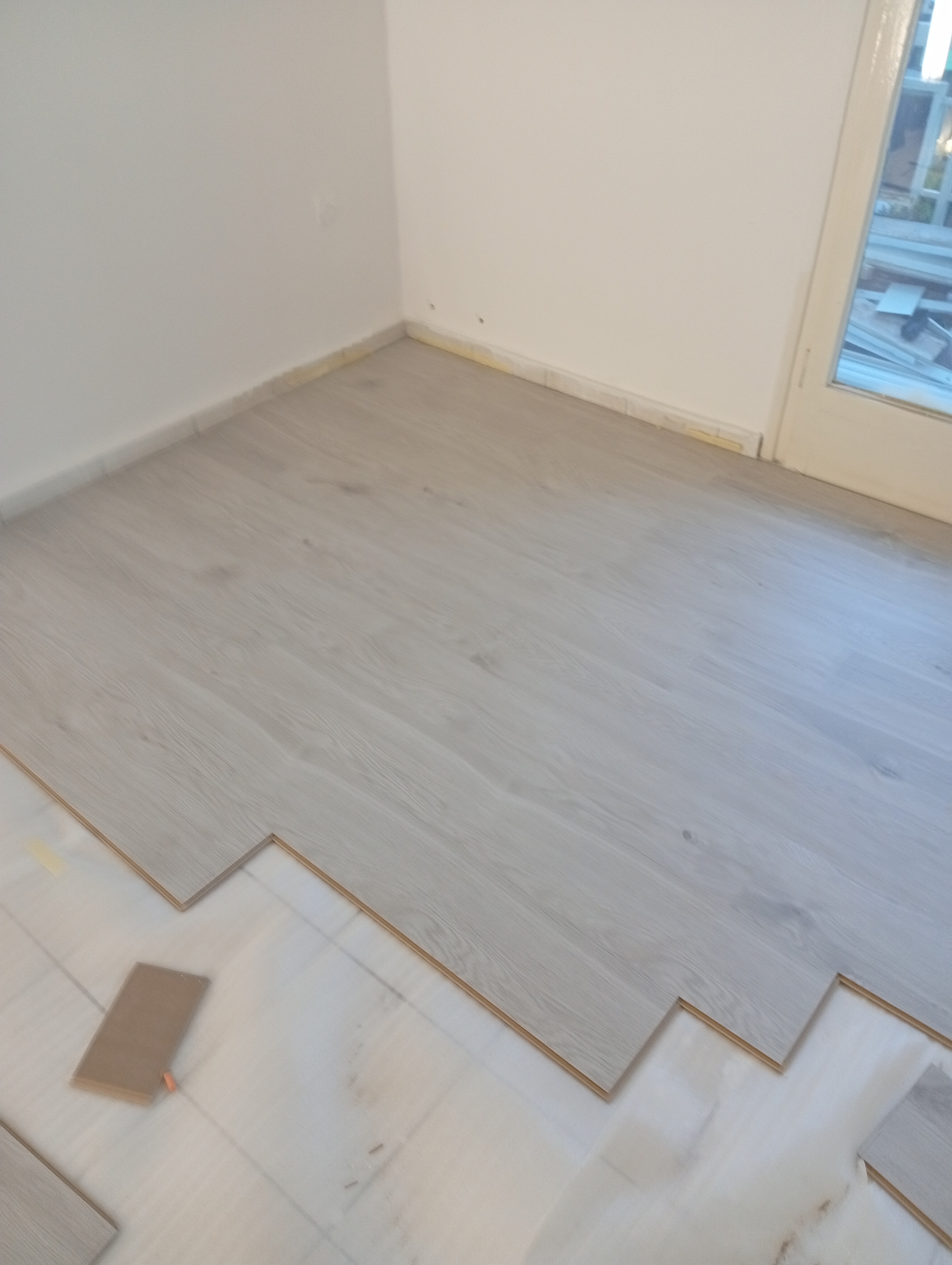 Μερικώς τοποθετημένο δάπεδο laminate σε ένα δωμάτιο, με ορισμένα πάνελ που δεν έχουν ακόμη τοποθετηθεί, που δείχνει τη μετάβαση από λευκά πλακάκια σε laminate με όψη ξύλου.