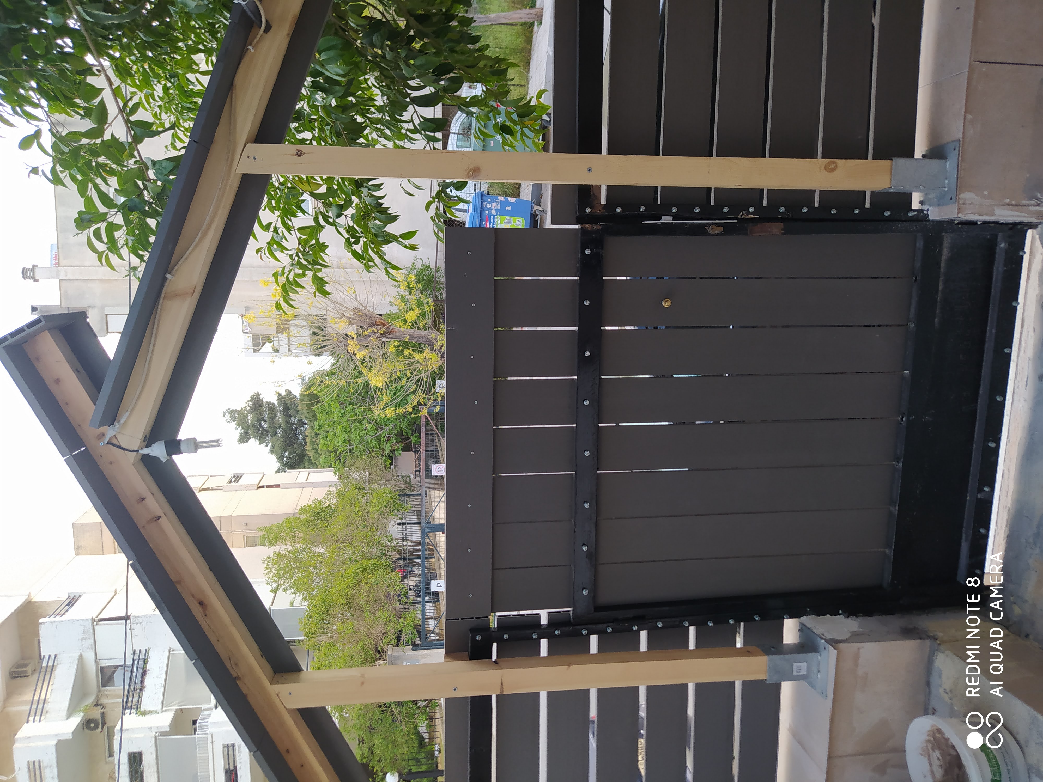 Μια ξύλινη πύλη με στέγαστρο πλαισιώνεται από έναν φράχτη και με δέντρα.